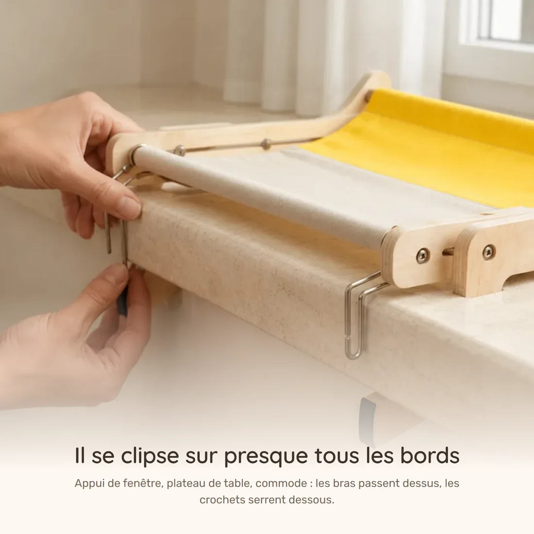 Il se clipse sur presque tous les bords — deux mains engagent les crochets du hamac à cadre bois sous un appui de fenêtre