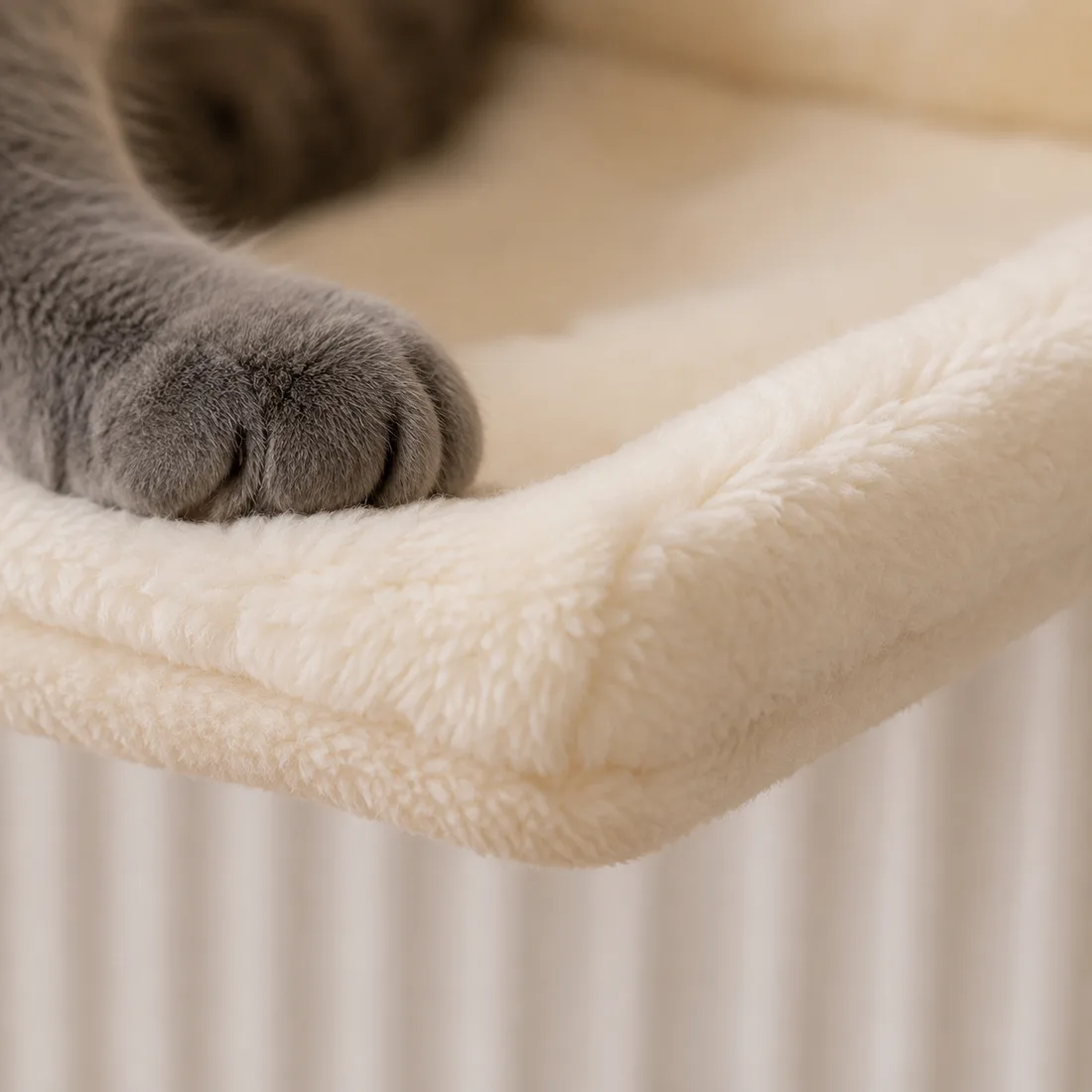 Macrophotographie du bord avant du hamac crème : couture périphérique, épaisseur de la peluche, une patte grise posée